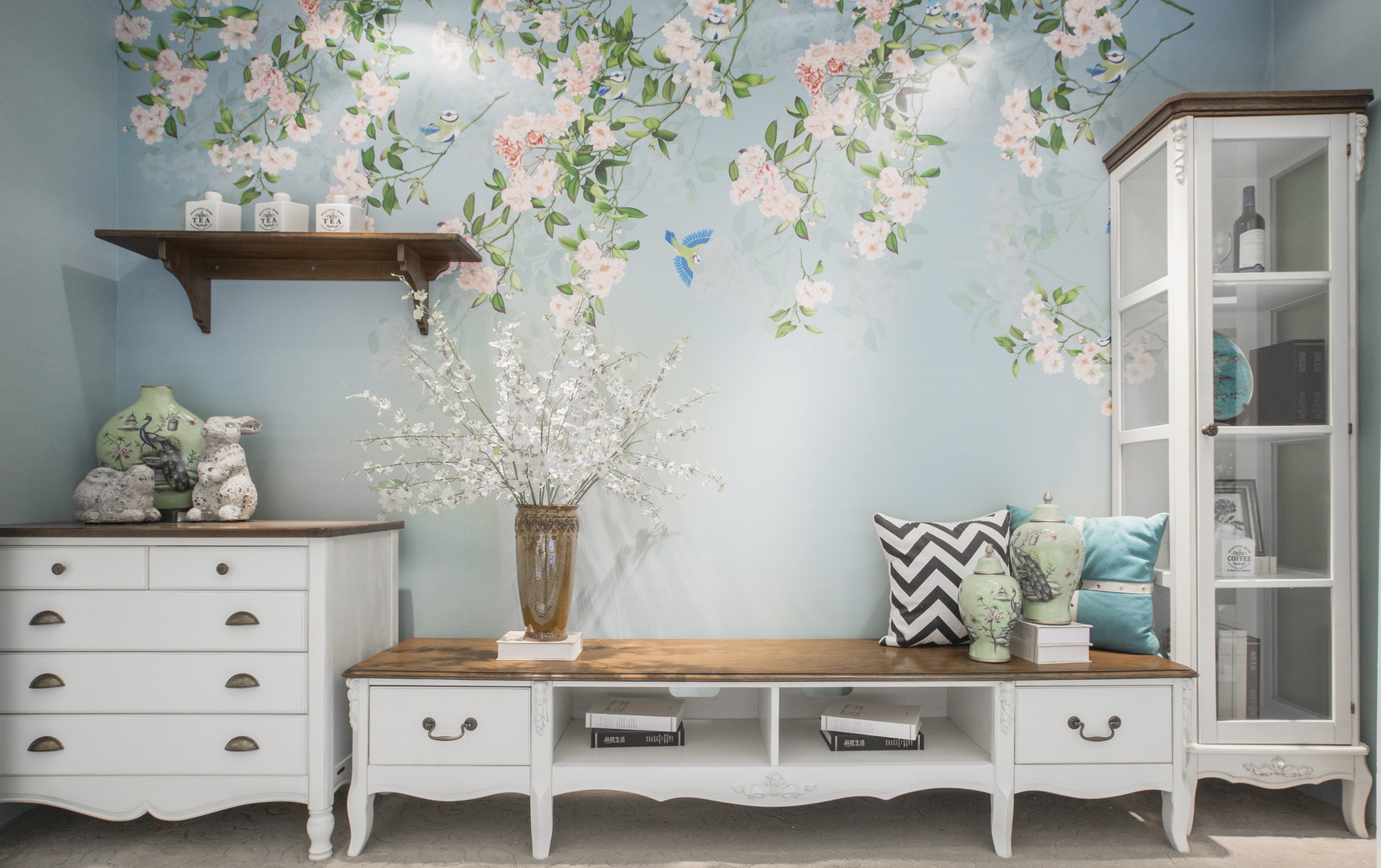 墙壁上的印花成了巨大的装饰，在一片繁花下，白色的家具显得洁净清爽。不同颜色的靠枕，桌上摆的饰物都让纯白显得不再单调。